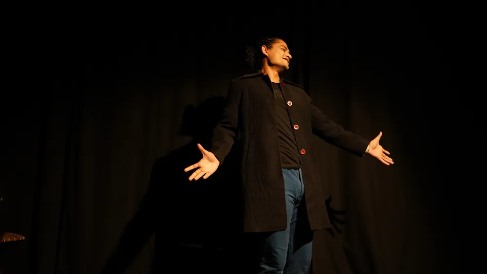 A performer opens his arms on a dark stage