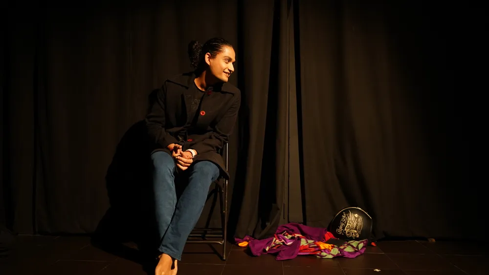 A performer sits beside a colourful cloth on stage
