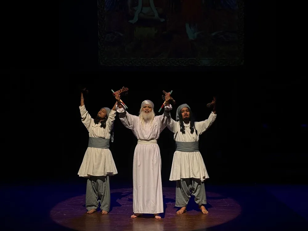Three performers in pale costumes on a dark stage